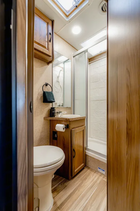 This compact RV rental bathroom showcases a toilet, wood vanity, and shower stall, offering essential amenities in a small space.. Coachman Prism 2200 LE 2017