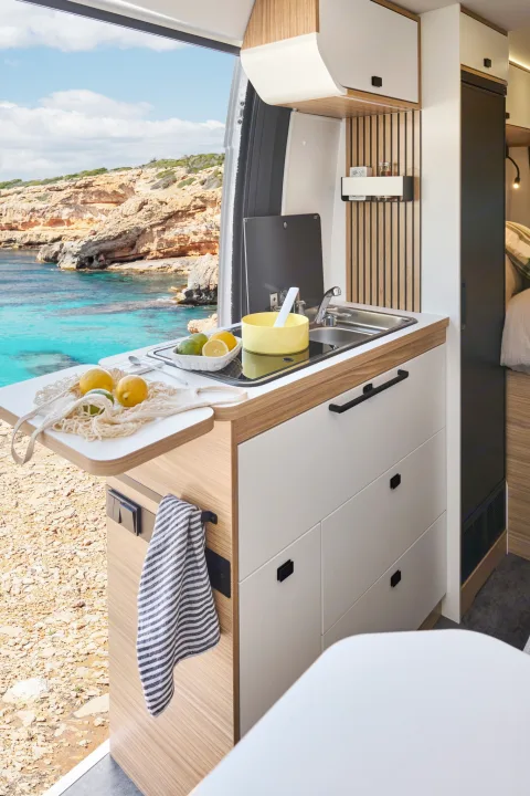 This rv rental features a compact kitchen inside a camper van, offering a stunning coastal view with turquoise water.. PILOTE V600G 2026
