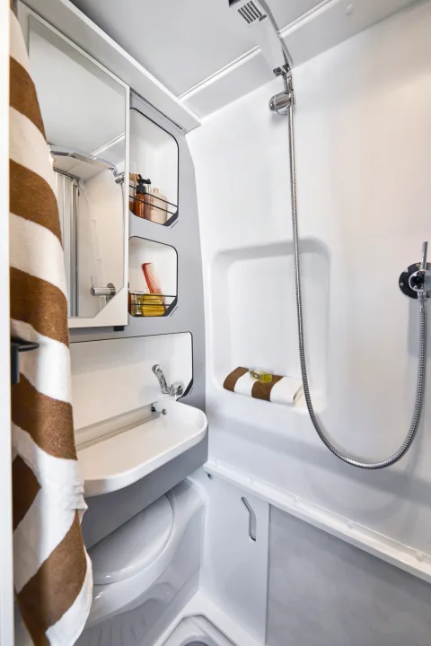 Compact RV rental bathroom: functional wet bath with shower, sink, toilet, and organized shelving for toiletries.. PILOTE V600G 2026