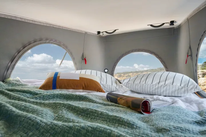 Cozy RV rental interior with a comfy bed, green blanket, pillows, and arched windows showing beautiful outdoor views.. PILOTE V600G 2026