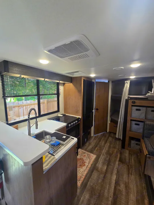 Spacious rv rental interior: modern kitchen, bunk beds, wood-look flooring, and ceiling AC unit.. Forest River Campsite Reserve 2025