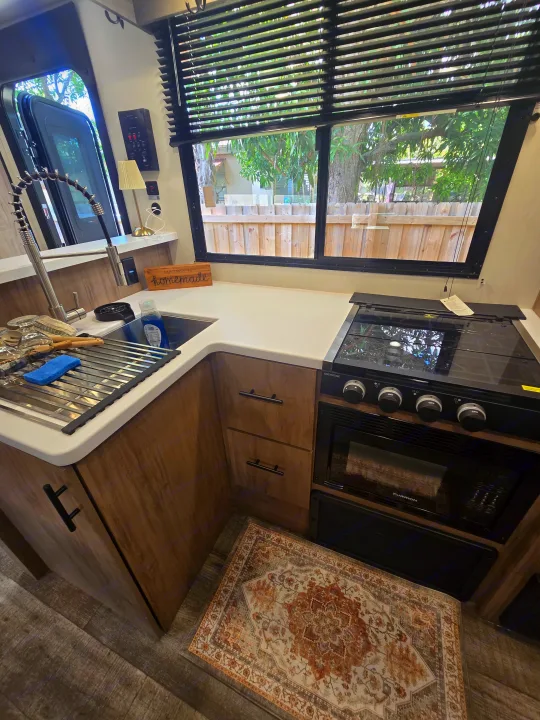 Compact RV rental kitchen with modern sink, Greystone stove, Furrion microwave, ample counter space, and warm wood cabinetry.. Forest River Campsite Reserve 2025