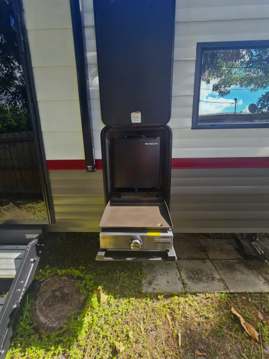 This RV rental features an outdoor kitchen with a Greystone griddle and RVISION screen, ideal for camping adventures.. Forest River Campsite Reserve 2025