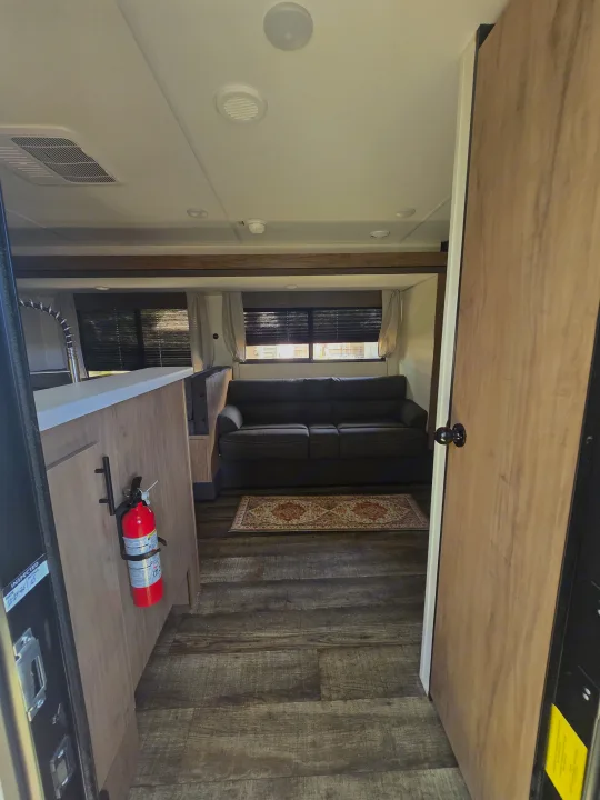 Welcome to your rv rental! View from the entry showing the living area, sofa, kitchen counter, and fire extinguisher.. Forest River Campsite Reserve 2025