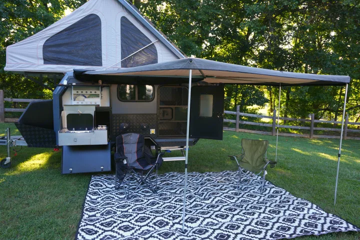 This RV rental camper trailer is set up for outdoor adventure, featuring an awning, pop-top tent, chairs, and an outdoor kitchen.. Zoomies Campers Spirit 2025