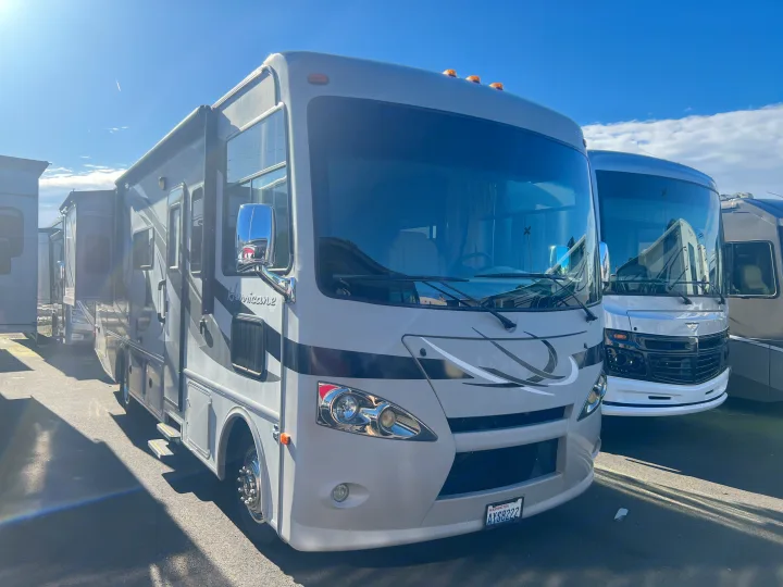 A large, light-colored Class A RV rental, a Hurricane motorhome, is parked with its side extended on a sunny day next to other RVs.. Thor Hurricane 2014