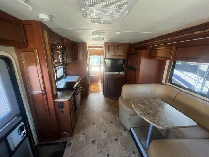 RV rental: Interior shows kitchen, dinette with U-shaped booth, and living area. Dark wood cabinets, light counters & flooring.. Thor Hurricane 2014