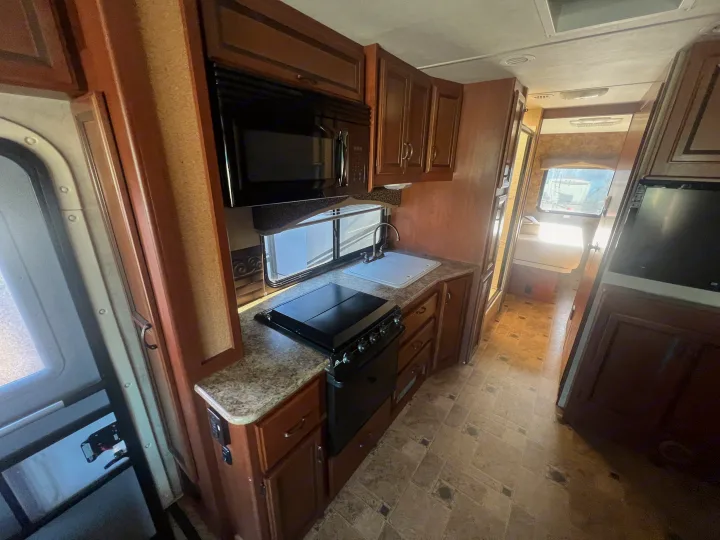 Explore this RV rental's cozy kitchen: microwave, stovetop, sink, and ample wood cabinetry in a compact space.. Thor Hurricane 2014