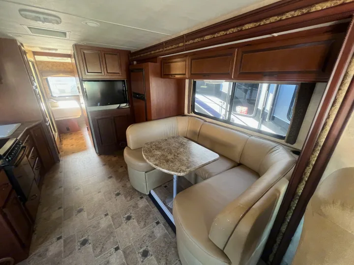 RV rental interior: light tan U-shaped dinette, speckled table, wood cabinets, and kitchen. A comfortable travel space.. Thor Hurricane 2014