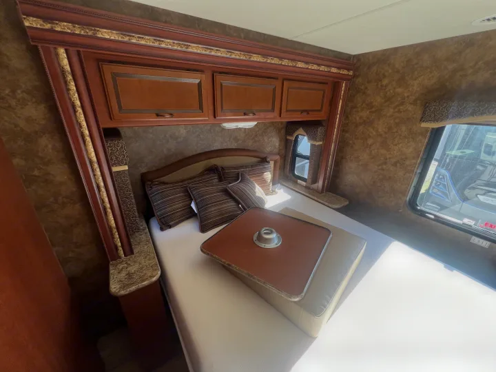 Inviting RV rental bedroom with a comfy bed, overhead storage, side table, window, and a removable bed table.. Thor Hurricane 2014