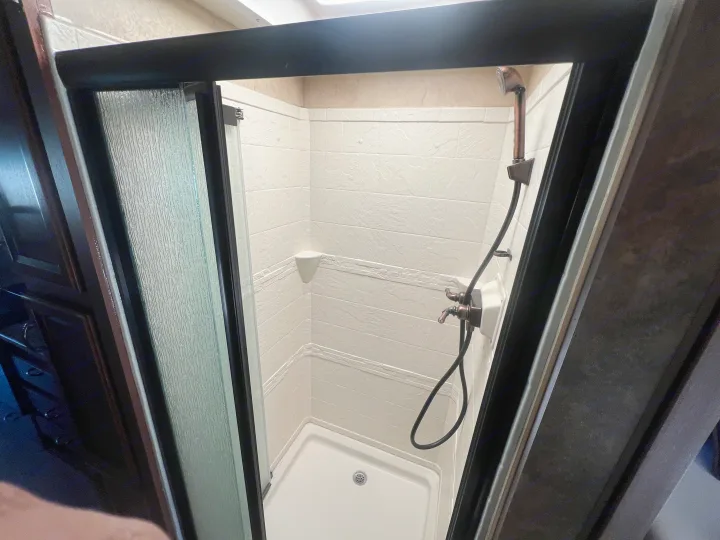 A clean, compact shower stall in an RV rental, with white textured walls, a modern shower head, and a clear sliding door.. Thor Hurricane 2014