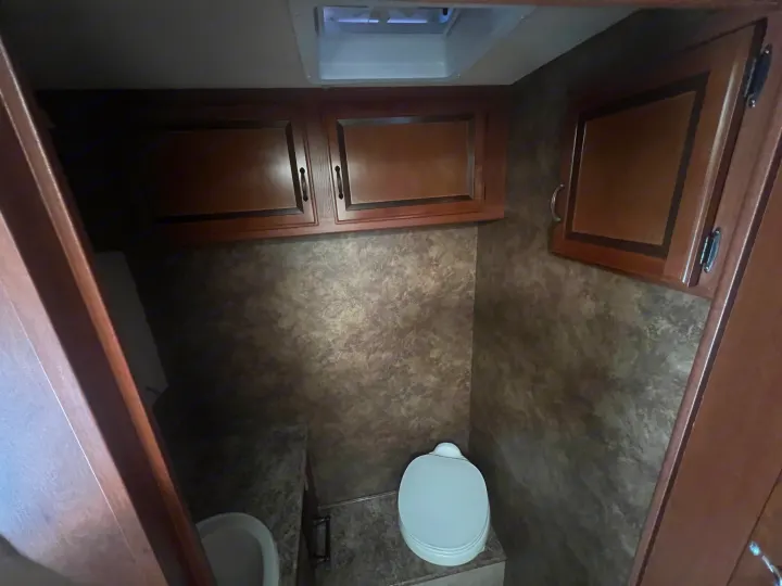 Compact RV rental bathroom with toilet, vanity, and overhead cabinets. Functional space for travel.. Thor Hurricane 2014
