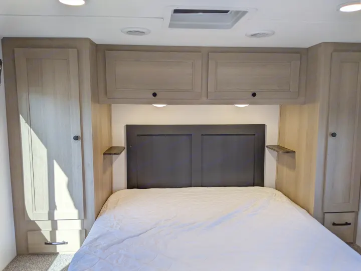 Comfortable RV rental bedroom featuring a bed, headboard, overhead cabinets, and side wardrobes for travel convenience.. Forest River Sunseeker 2025