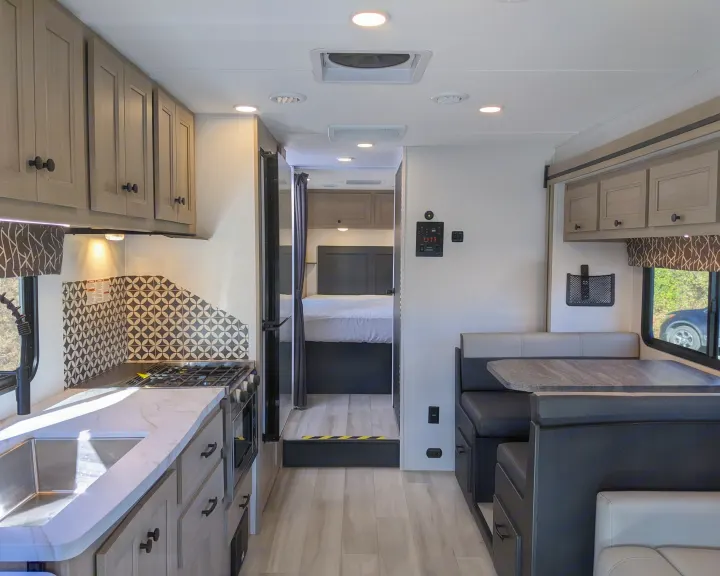 Bright RV rental interior: modern kitchen, dinette, and bedroom view. Features light wood cabinets, patterned backsplash.. Forest River Sunseeker 2025