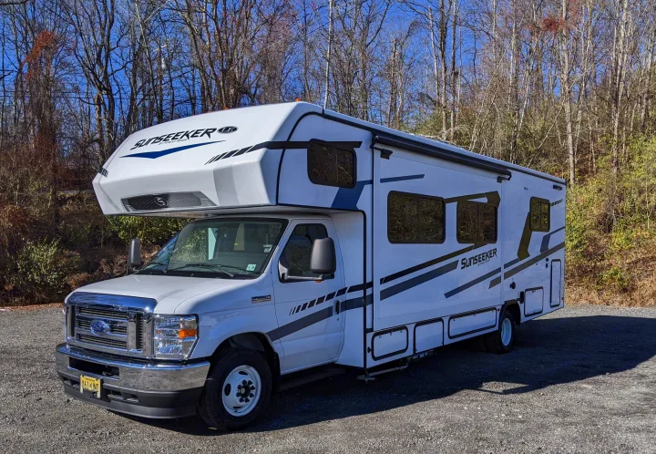 White Sunseeker Class C rv rental parked on a gravel lot under a blue sky, with bare trees in the background.. Forest River Sunseeker 2025