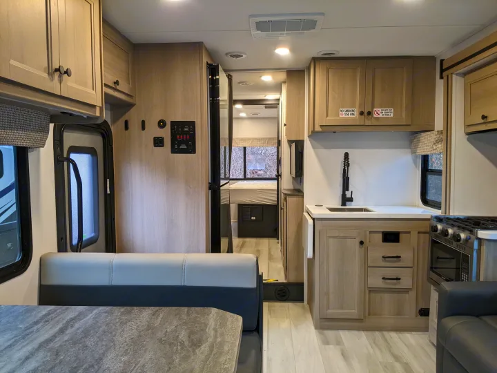 This rv rental features a clean, modern RV interior with a kitchen, dining area, and a glimpse of the bedroom.. Forest River Sunseeker 2025