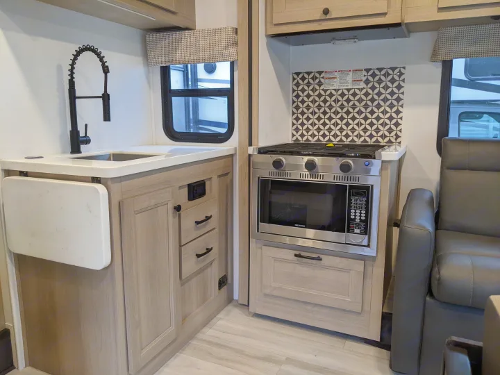 Explore this RV rental's functional kitchen: sink, black faucet, stovetop, oven, microwave, and pull-out counter.. Forest River Sunseeker 2025