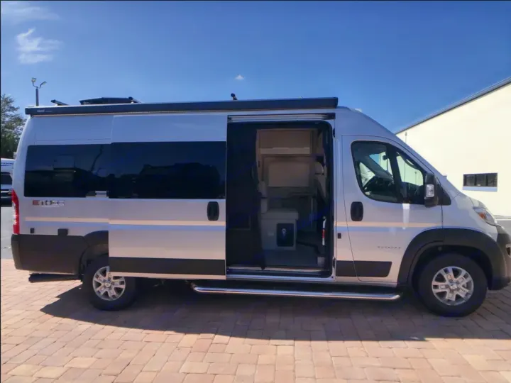 Silver camper van rv rental parked with its side door open, revealing the interior. An awning is extended above the door.. Entegra Coach Ethos 2025