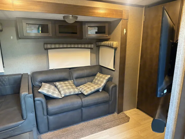 Inside your RV rental: a cozy living area with a gray leather sofa, decorative pillows, overhead storage, and window shades.. Forest River Flagstaff Classic 2020