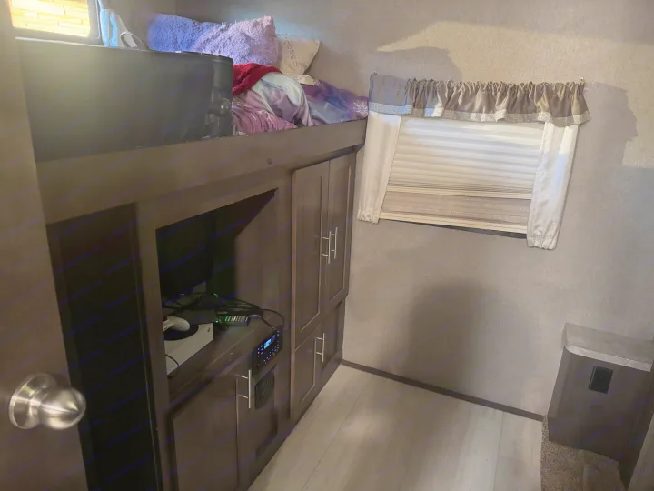 An RV rental's compact living space: bunk bed, entertainment center with game console, and window with blinds.. Forest River Flagstaff Classic 2020