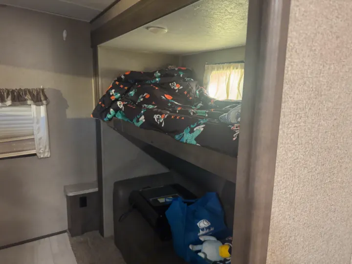 RV rental interior: a view of bunk beds. The upper bunk has a patterned duvet, and below is a seating area with a bag.. Forest River Flagstaff Classic 2020