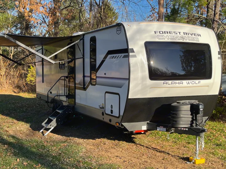 A sleek Forest River Cherokee Alpha Wolf travel trailer, ideal for your next RV rental adventure, parked among autumn trees.. Forest River Cherokee Alpha Wolf 2025