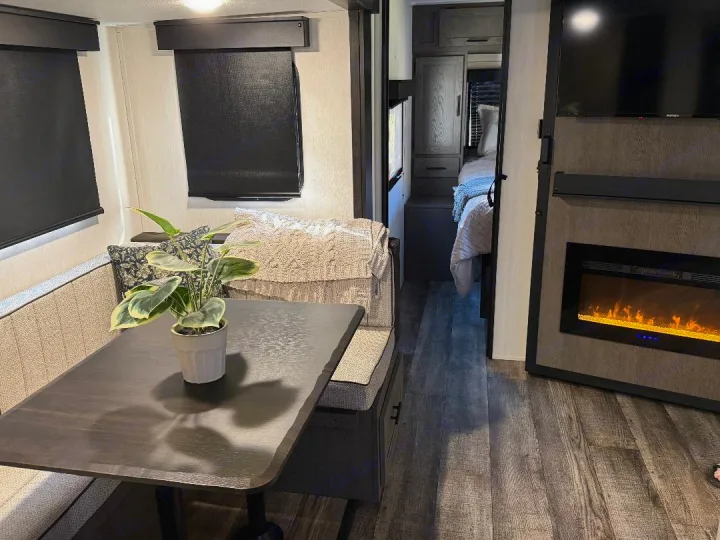 Comfortable RV rental interior: dining booth, glowing electric fireplace, and cozy bedroom. Your modern home on wheels awaits.. Forest River Cherokee Alpha Wolf 2025