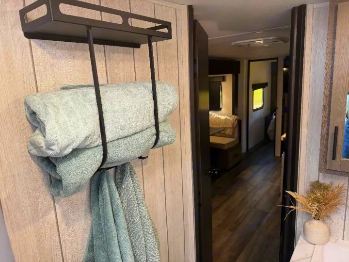 Inside a spacious RV rental: a bathroom wall with towels on a black rack, looking down the interior hall.. Forest River Cherokee Alpha Wolf 2025