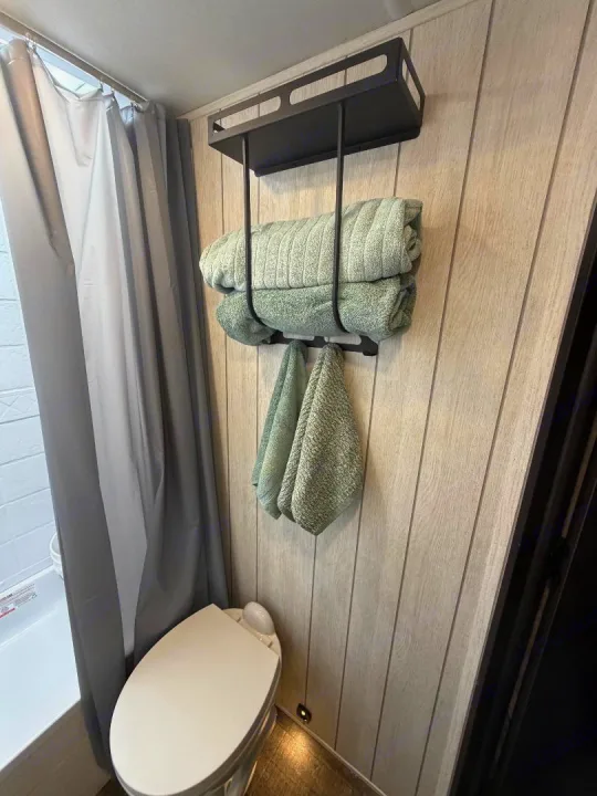 Compact RV rental bathroom with shower, toilet, and clever wall-mounted storage for green towels, maximizing space efficiently.. Forest River Cherokee Alpha Wolf 2025