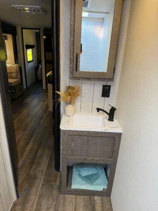 Modern RV rental bathroom with a vanity, sink, mirror, and light blue towels, overlooking the RV's hallway.. Forest River Cherokee Alpha Wolf 2025