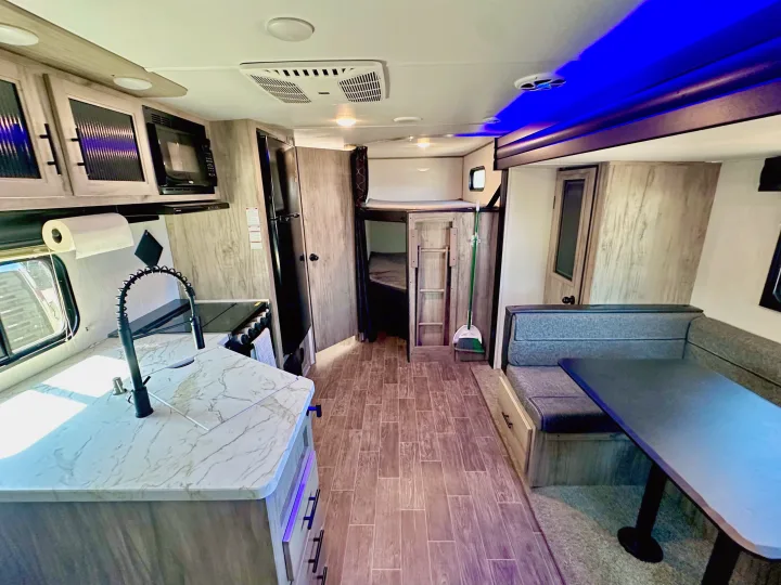 Spacious rv rental interior showing kitchen with sink/stove, dining booth, and bunk beds, illuminated by modern blue lights.. Forest River Cherokee Alpha Wolf 2022