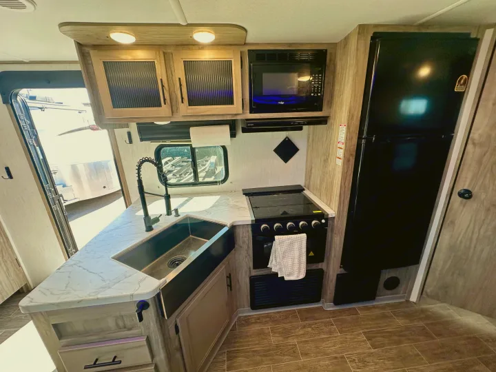 Modern RV rental kitchen featuring a large black sink, stove, microwave, and full-size refrigerator for your travels.. Forest River Cherokee Alpha Wolf 2022