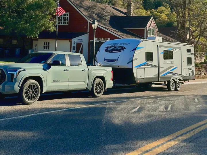 Sage green pickup towing a gray Alpha Wolf RV rental by a museum. Ready for a scenic road trip adventure.. Forest River Cherokee Alpha Wolf 2022
