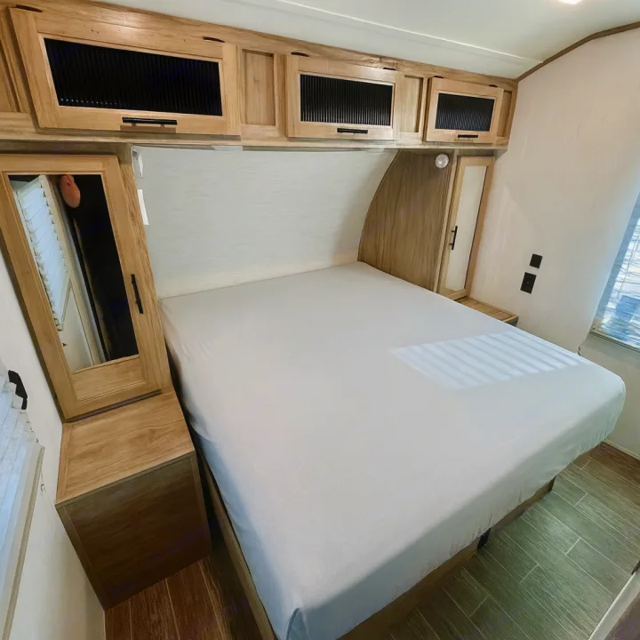 This rv rental bedroom shows a comfortable bed, overhead storage, and mirrored cabinets in a compact interior.. Forest River Cherokee Alpha Wolf 2022