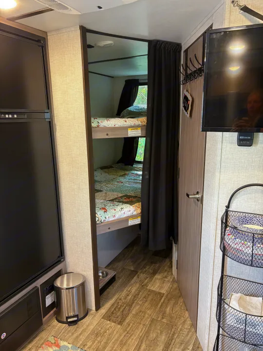 Cozy RV rental bunk bed area, featuring a fridge, TV, coat rack, and pet station. Ideal for family camping.. Crossroads RV Sunset Trail Super Lite 2021