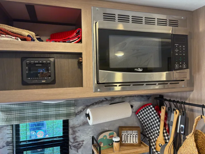 RV rental kitchen showing built-in microwave, Jensen stereo, paper towels, and hanging cooking utensils on wall.. Crossroads RV Sunset Trail Super Lite 2021