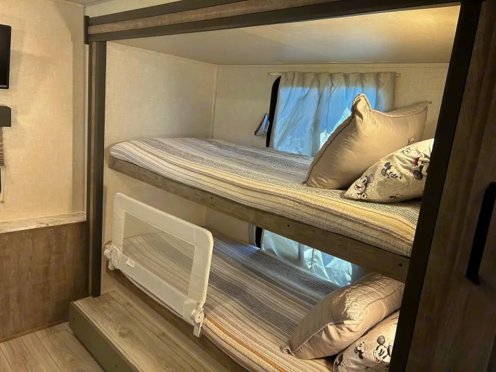 Inside an RV rental: cozy bunk beds with a safety rail, perfect for family adventures. Mickey Mouse pillows add a fun touch.. Forest River Surveyor 2023
