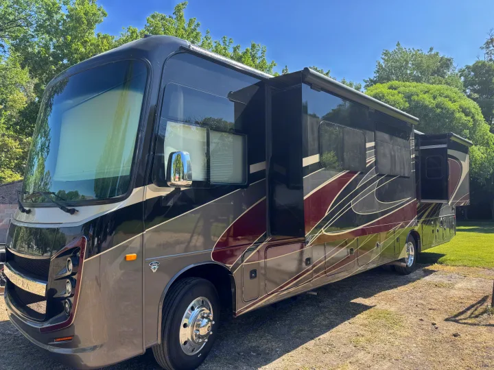 Modern dark Integra RV rental with extended slide-outs, parked outdoors against a clear sky and trees.. Entegra Coach Vision XL 2021