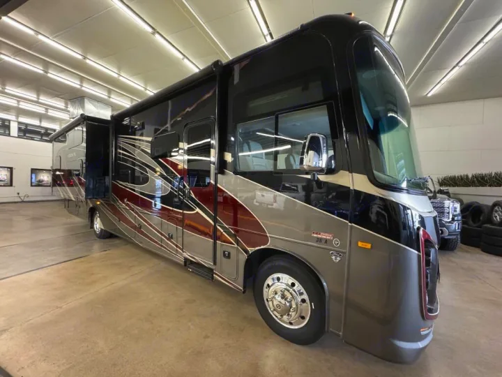 Luxury RV rental: A modern black, grey, and maroon motorhome with extended slides, parked indoors.. Entegra Coach Vision XL 2021