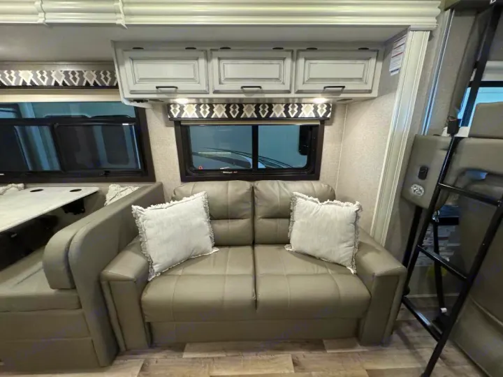 Modern RV rental living space featuring a comfy gray sofa with pillows, overhead cabinets, a dinette, and bunk beds.. Entegra Coach Vision XL 2021