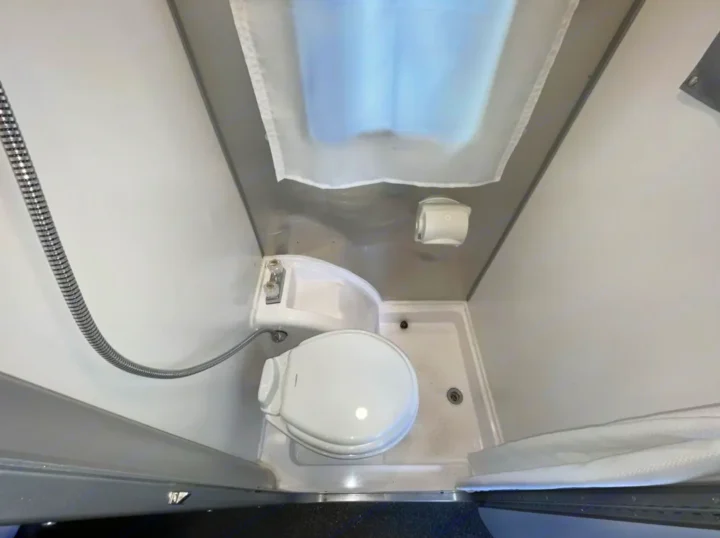 Compact RV rental wet bath features a toilet, corner sink, and shower head. All-in-one design for travelers' convenience.. Airstream Basecamp 2022