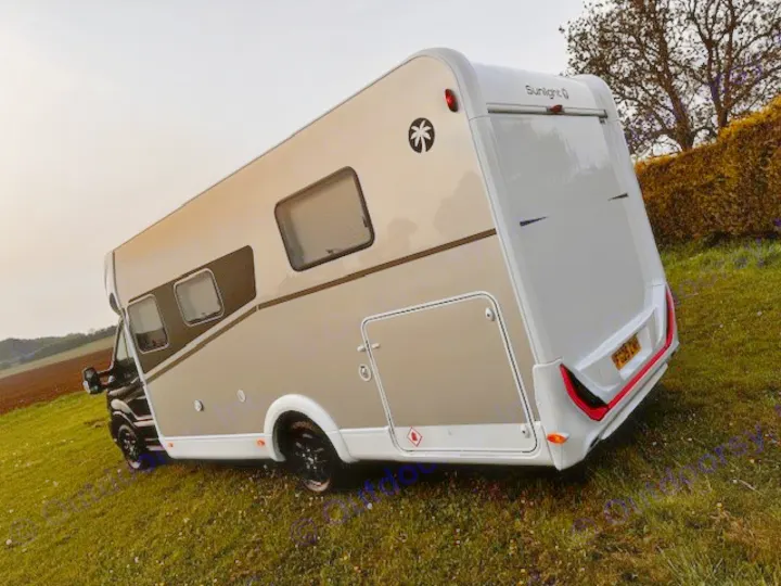 This Sunlight motorhome, ideal for an RV rental adventure, is parked tilted on a grassy hill under an overcast sky.. Sunlight T690L 2025
