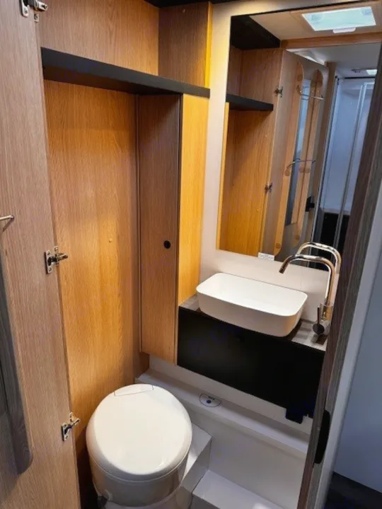 Inside an RV rental: a neat bathroom with a modern sink, toilet, mirror, and accessible shower area.. Sunlight T690L 2025