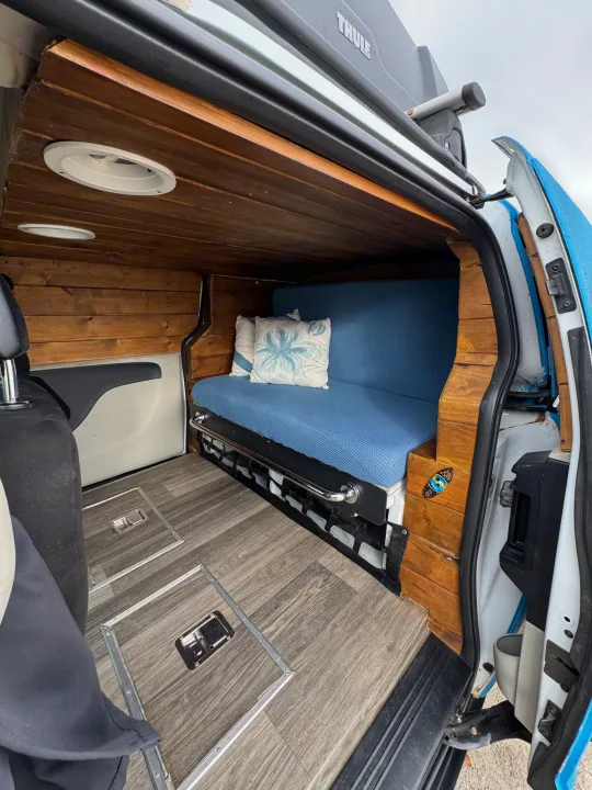Cozy van interior for your next rv rental adventure! Features wood paneling, comfy blue bench, and floor storage.. Ram C/V Tradesman 2014