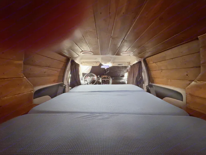 Cozy rv rental interior: wood-paneled camper van bedroom with a soft bed, looking toward the dashboard.. Ram C/V Tradesman 2014