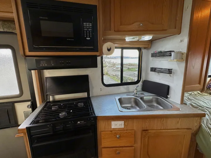 Explore this functional rv rental kitchen featuring a microwave, stove, sink, and a beautiful window view of the waterfront.. Ford E350 Travelmaster 1997