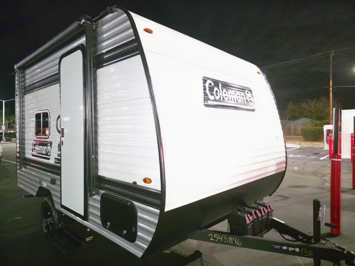 This white and gray Coleman RV rental, a small travel trailer, is parked at night, ready for camping or road trips.. KEYSTONE COLEMAN 13B 2026
