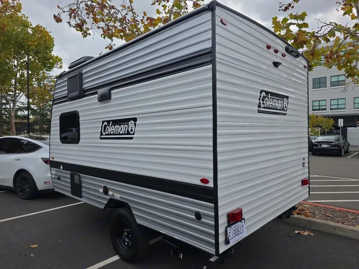 Grey and black Coleman travel trailer hitched to a white Tesla in a parking lot. An ideal RV rental for road trips.. KEYSTONE COLEMAN 13B 2026