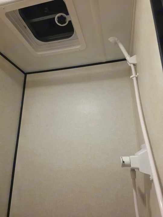Inside an RV rental shower: light textured walls, white showerhead, and a crank-operated roof vent for ventilation.. KEYSTONE COLEMAN 13B 2026