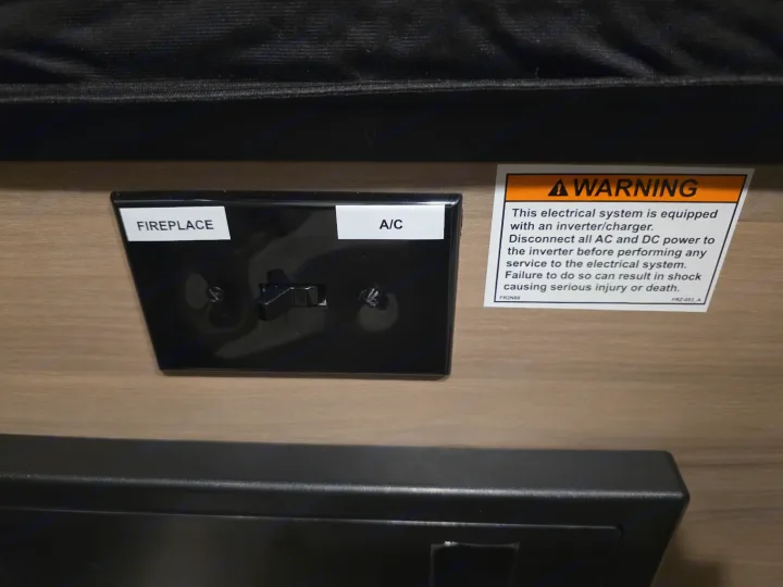RV rental interior: an electrical panel with 'Fireplace' and 'A/C' switches, and a critical electrical safety warning.. KEYSTONE COLEMAN 13B 2026